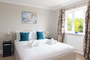 A bedroom with a bed, pillows, a nightstand, a lamp, a painting, and a window with curtains. - Spacious Sidlesham Country Home Near Witterings (Chichester)
