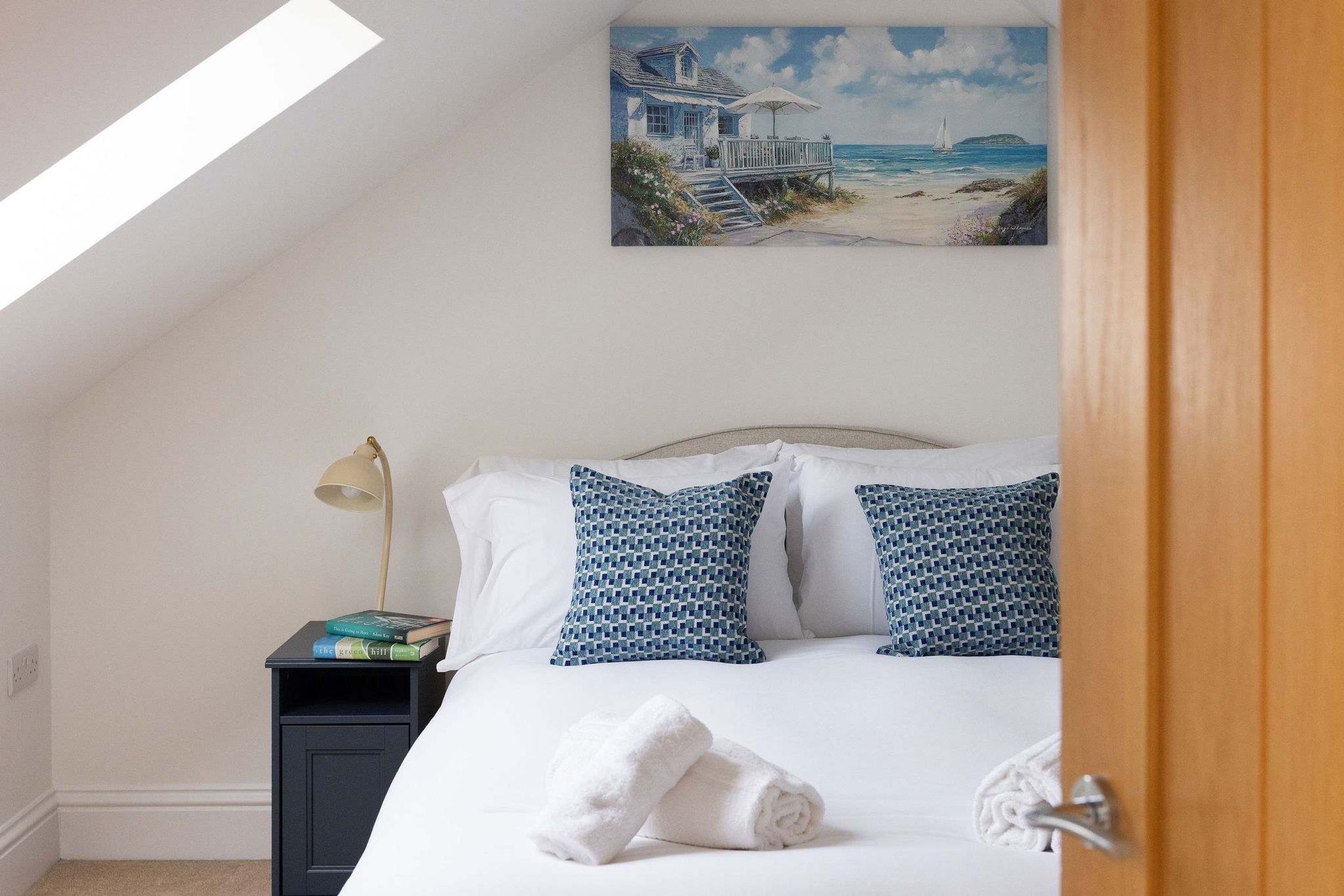 Une chambre à coucher avec un lit, des oreillers, une table de chevet, une lampe, un tableau et une serviette.