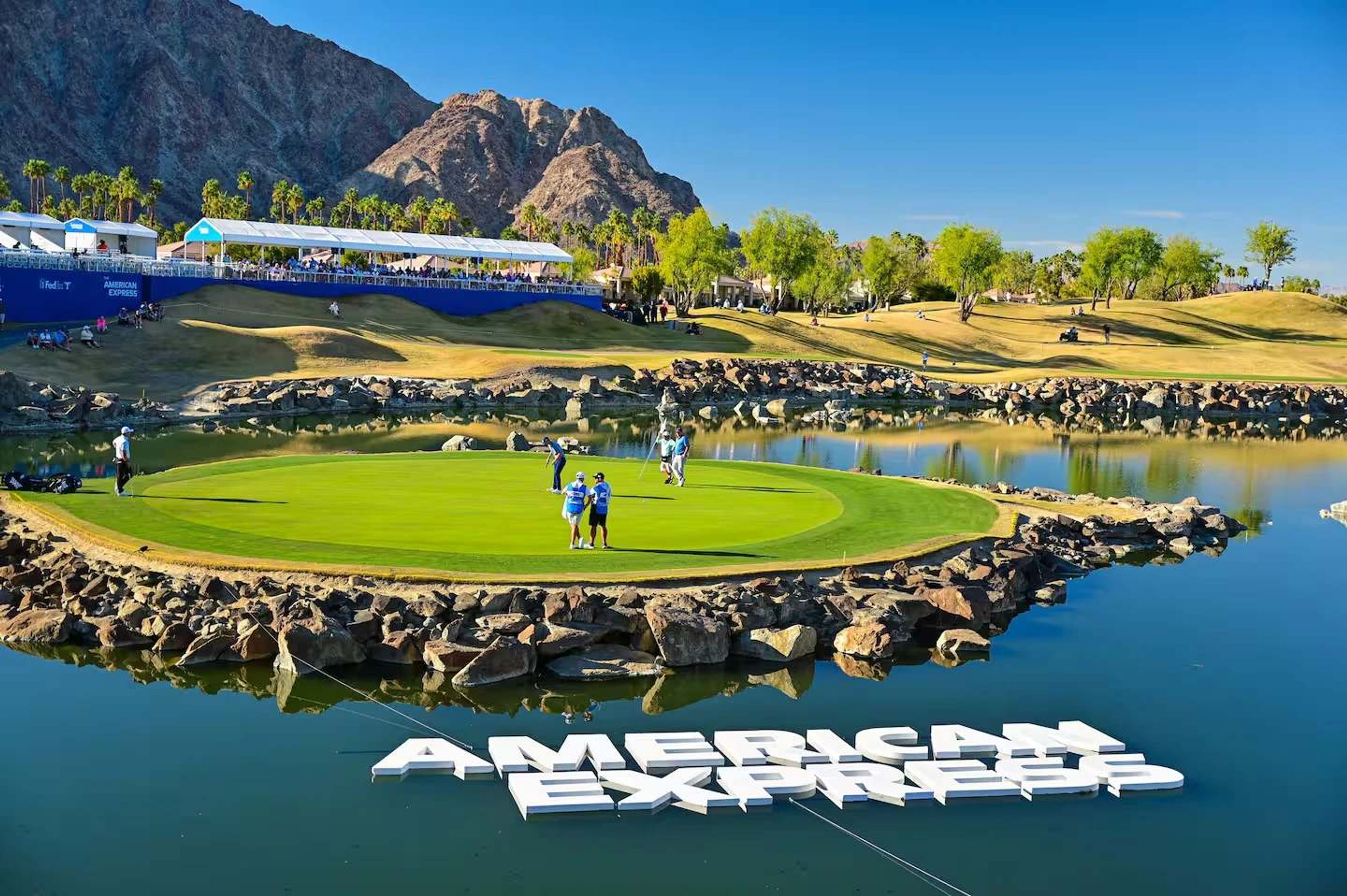 Golfkenttä, jossa on lampi, taustalla vuori ja American Express -logon kuva vedessä.