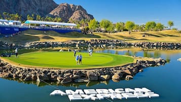 Golfkenttä, jossa on lampi, taustalla vuori ja American Express -logon kuva vedessä.