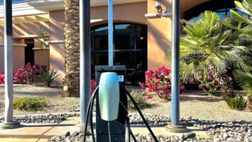 A parking area with a charging station, palm trees, and a building labeled 'BASSY SUITES' in the background.