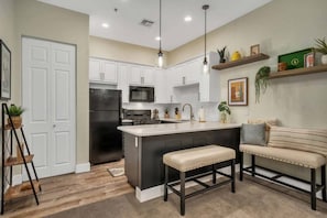 A modern kitchen with white cabinets, a black refrigerator, a microwave, and a central island with stools. - Casa Arenas Modern Desert Retreat in Old Town LQ (La Quinta)