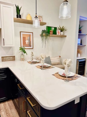 A kitchen with a white countertop, black cabinets, and a hanging light fixture. - Casa Arenas Modern Desert Retreat in Old Town LQ (La Quinta)
