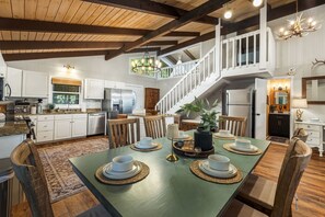 Eine geräumige Küche mit modernen Geräten, ein Essbereich mit einem grünen Tisch und eine Treppe, die zu einer oberen Ebene führt.