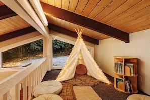Una habitación acogedora con techo de madera, una estructura parecida a una tienda con luces, una estantería y una ventana con vistas a un paisaje natural.