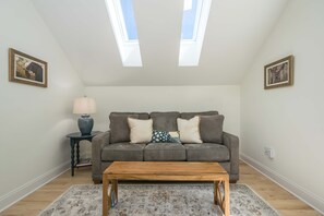 A living room with a grey sofa, a wooden coffee table, a patterned rug, and two skylights. - 2BR Saluda Townhome Elevator Free Tix (Saluda)