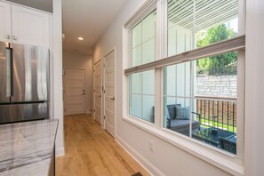 A kitchen with a stainless steel refrigerator, a hallway with white doors, and a large window overlooking a patio with outdoor furniture. - 2BR Saluda Townhome Elevator Free Tix (Saluda)