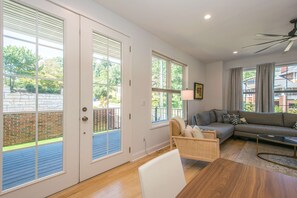 A living room with a sofa, a chair, a coffee table, and a floor lamp. There are large windows with blinds, a door, and a view of the outside. - 2BR Saluda Townhome Elevator Free Tix (Saluda)