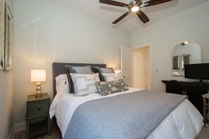 A bedroom with a bed, a nightstand, a lamp, a ceiling fan, a television, and a door. - 2BR Saluda Townhome Elevator Free Tix (Saluda)