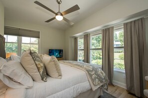 A bedroom with a bed, pillows, a ceiling fan, a television, and large windows with curtains. - 2BR Saluda Townhome Elevator Free Tix (Saluda)