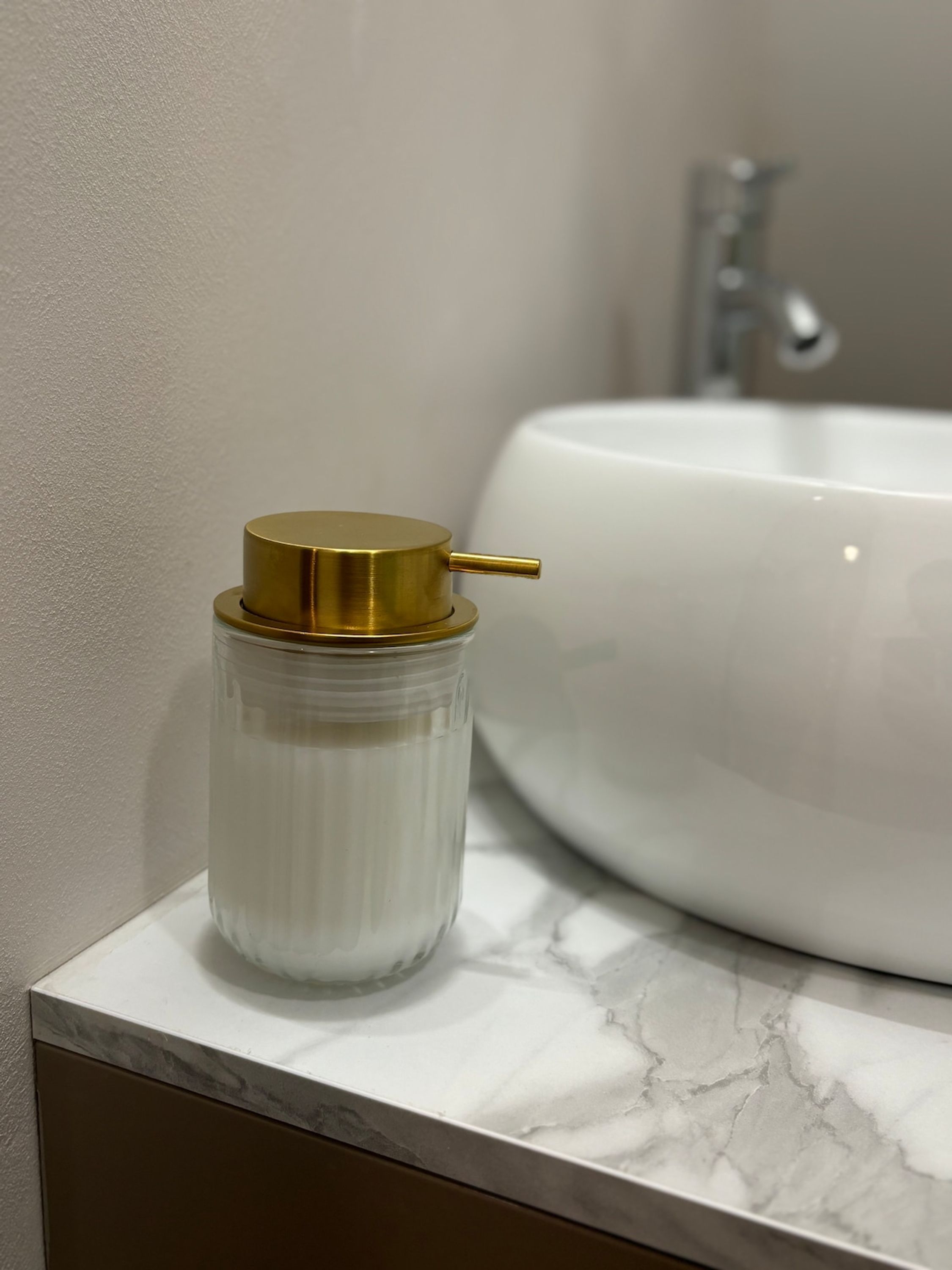A bathroom with a white sink and a glass container with a gold lid on a marble countertop.
