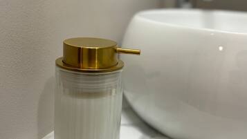 A bathroom with a white sink and a glass container with a gold lid on a marble countertop.