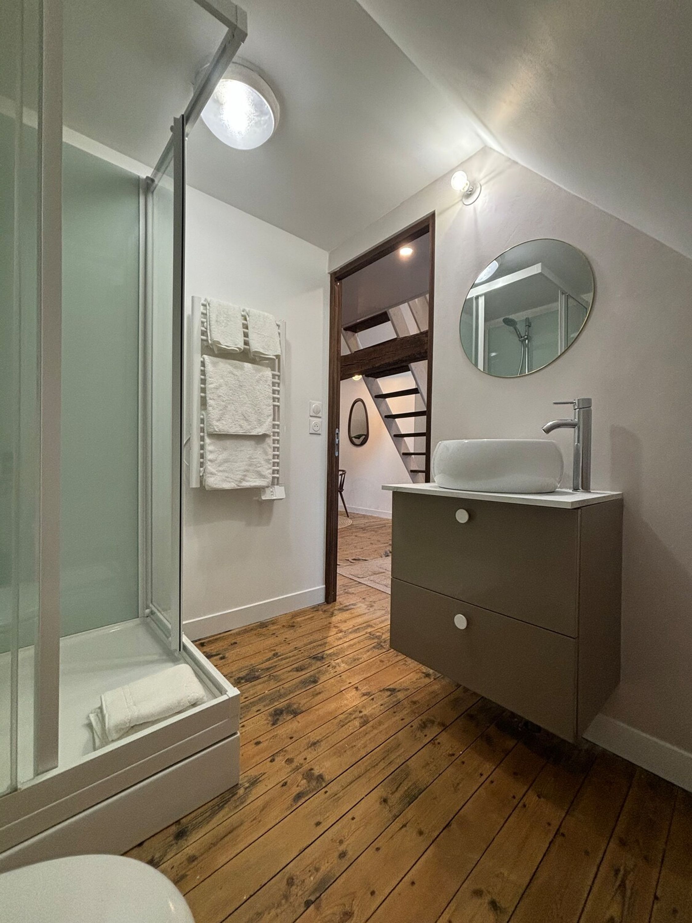 Un baño moderno con cabina de ducha de vidrio, un lavabo blanco y suelo de madera.