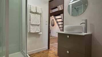 Un baño moderno con cabina de ducha de vidrio, un lavabo blanco y suelo de madera.