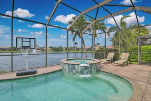 An outdoor swimming pool with a hot tub, surrounded by a metal fence, with a basketball hoop and chairs. - Sunny Lakeview Pool & Spa Retreat in South Fort Myers (Fort Myers)