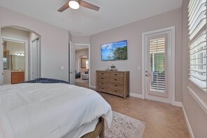 Un dormitorio con cama, cómoda, televisor en la pared y una puerta con persianas.