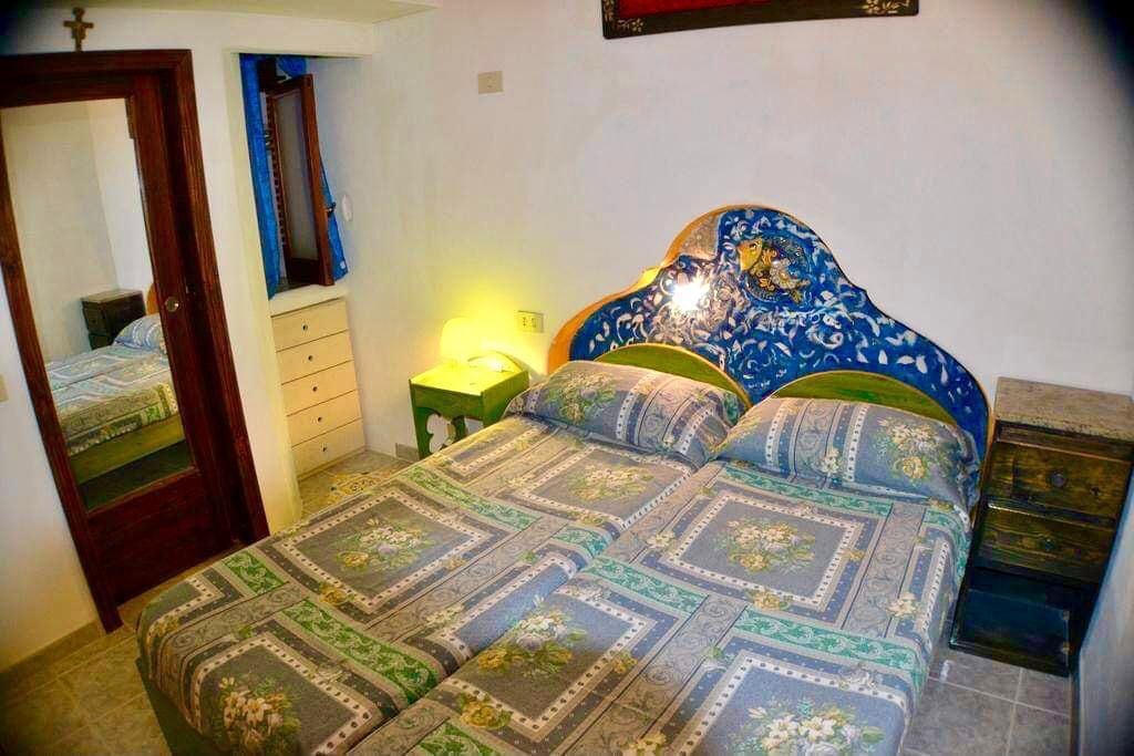 Een slaapkamer met een bed, nachtkastje, dressoir, spiegel en een wandlamp.