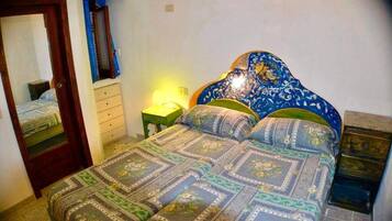 Een slaapkamer met een bed, nachtkastje, dressoir, spiegel en een wandlamp.