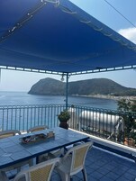 Una terraza con mesa y sillas, con vistas a la costa, una montaña y el mar.