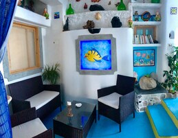 Una habitación con muebles de mimbre, un cuadro de un pez y varios objetos decorativos en estantes.