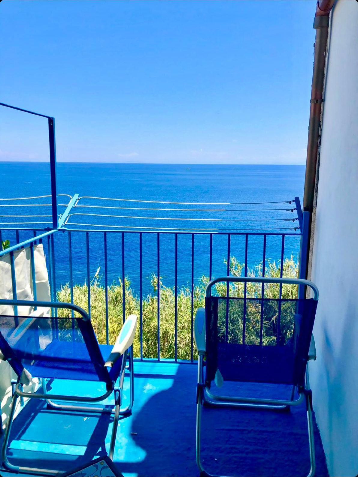 A balcony with two chairs, a railing, and a view of the sea.