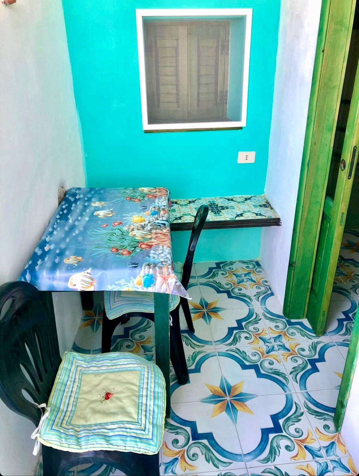 Een kleine kamer met een tafel, stoelen, een raam en vloertegels met een patroon.