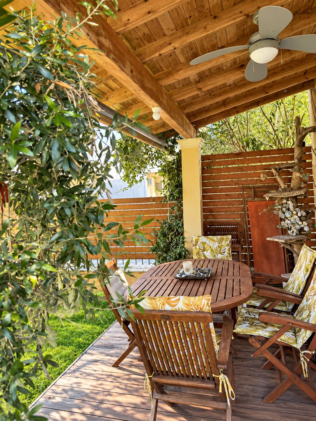 An outdoor wooden deck with a round table and chairs, a ceiling fan, and a wooden fence.