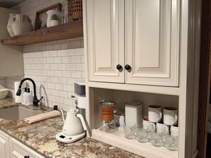 A kitchen with white cabinets, a granite countertop, a coffee maker, and a set of clear glasses.