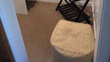 Un cuarto de lavandería con una silla negra, un banco blanco y estantes que contienen una cafetera, mancuernas y una cesta.