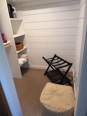 A laundry room with a black chair, a white bench, and shelves containing a coffee maker, dumbbells, and a basket.