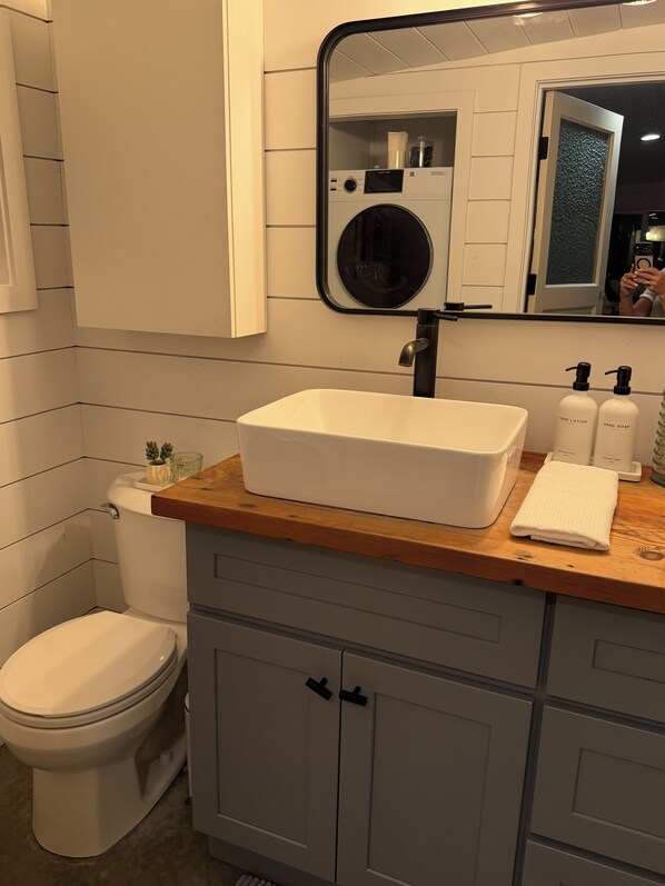A bathroom with a white sink, a mirror, a toilet, and a wooden countertop.