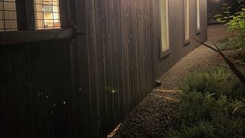 A wooden house with a covered porch, string lights, and a gravel path.
