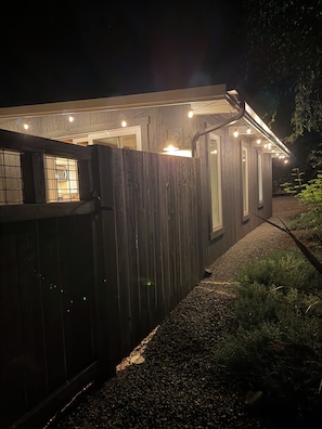 A wooden house with a covered porch, string lights, and a gravel path.