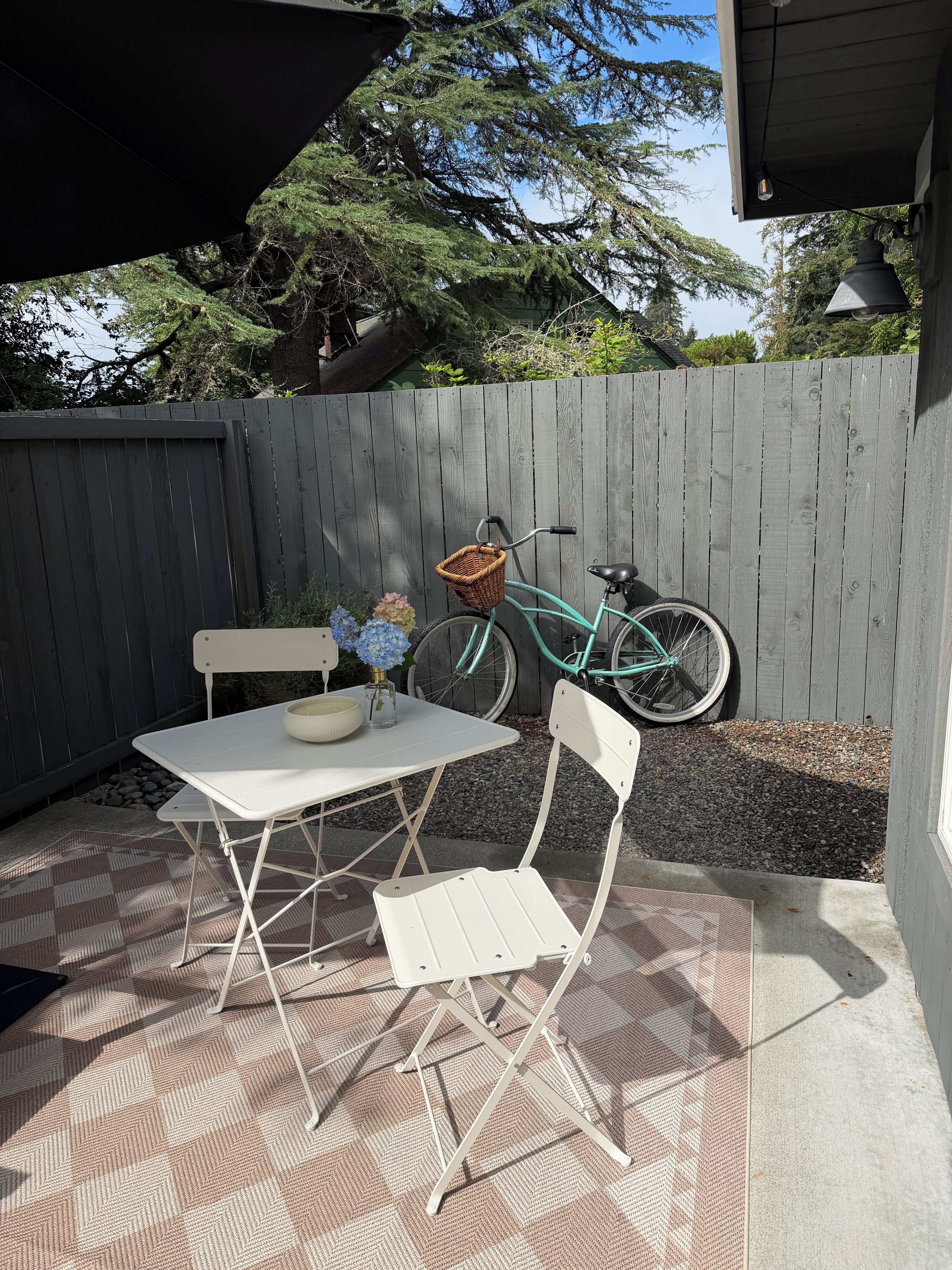 A patio with a white table and chairs, a wicker basket, and a bicycle.