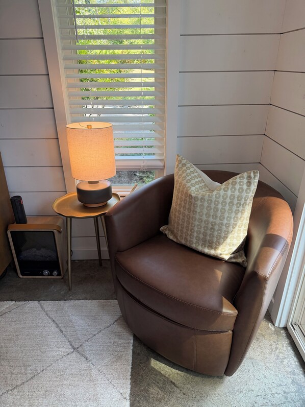 A corner room with a brown leather chair, a small table with a lamp, and a television.