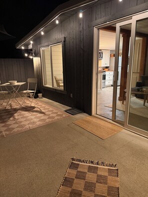 A covered outdoor seating area with a table and chairs, a rug, and a door leading to a kitchen.