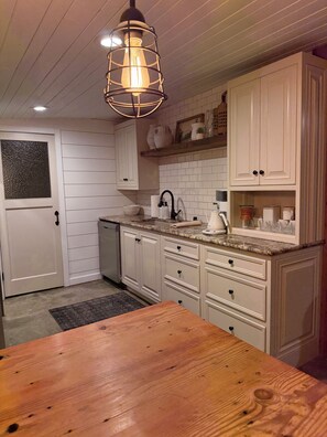 A kitchen with white cabinets, a wooden table, and a hanging light fixture.