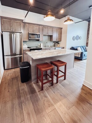 Una cocina moderna con electrodomésticos de acero inoxidable, taburetes de madera y una isla grande.