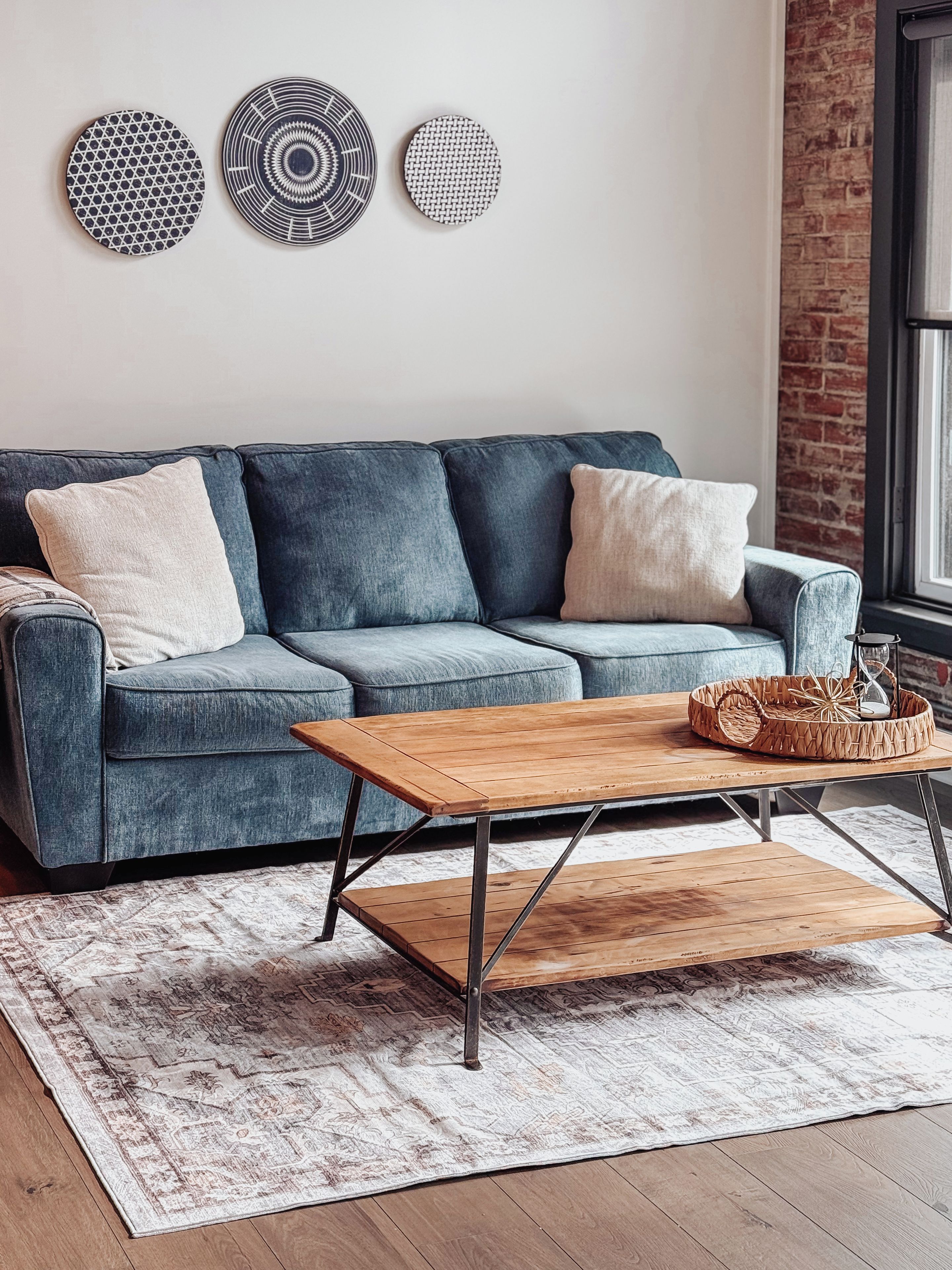 A living room with a blue sofa, a wooden coffee table, and a patterned rug.