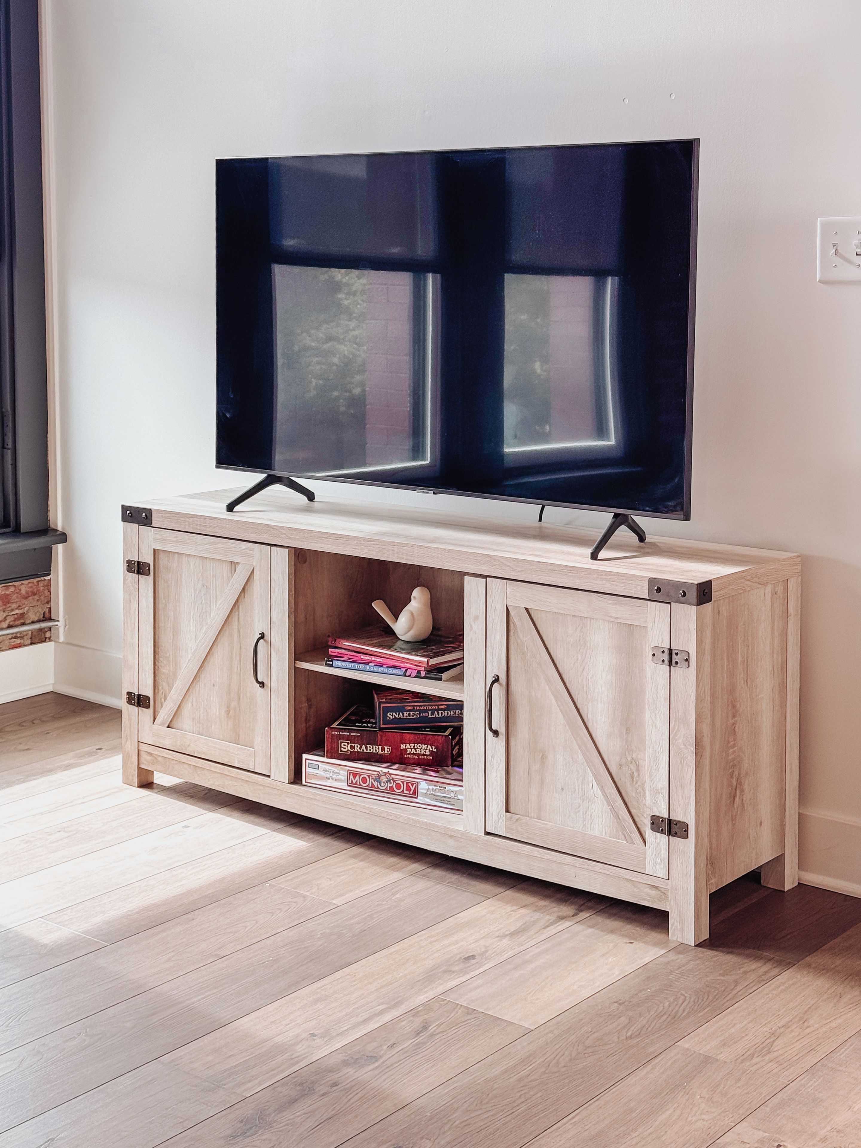 A wooden TV stand with a flat-screen TV mounted above it, featuring a window with blinds.