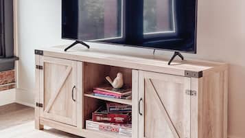 A wooden TV stand with a flat-screen TV mounted above it, featuring a window with blinds.