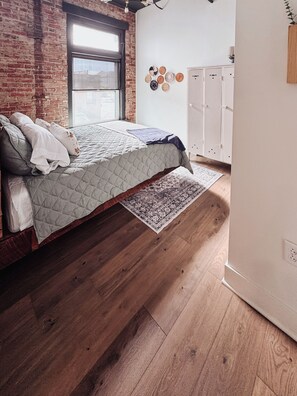 Un dormitorio con cama, suelo de madera, ventana y armario.
