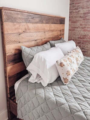 A bed with a wooden headboard, a quilted grey bedspread, and two pillows.
