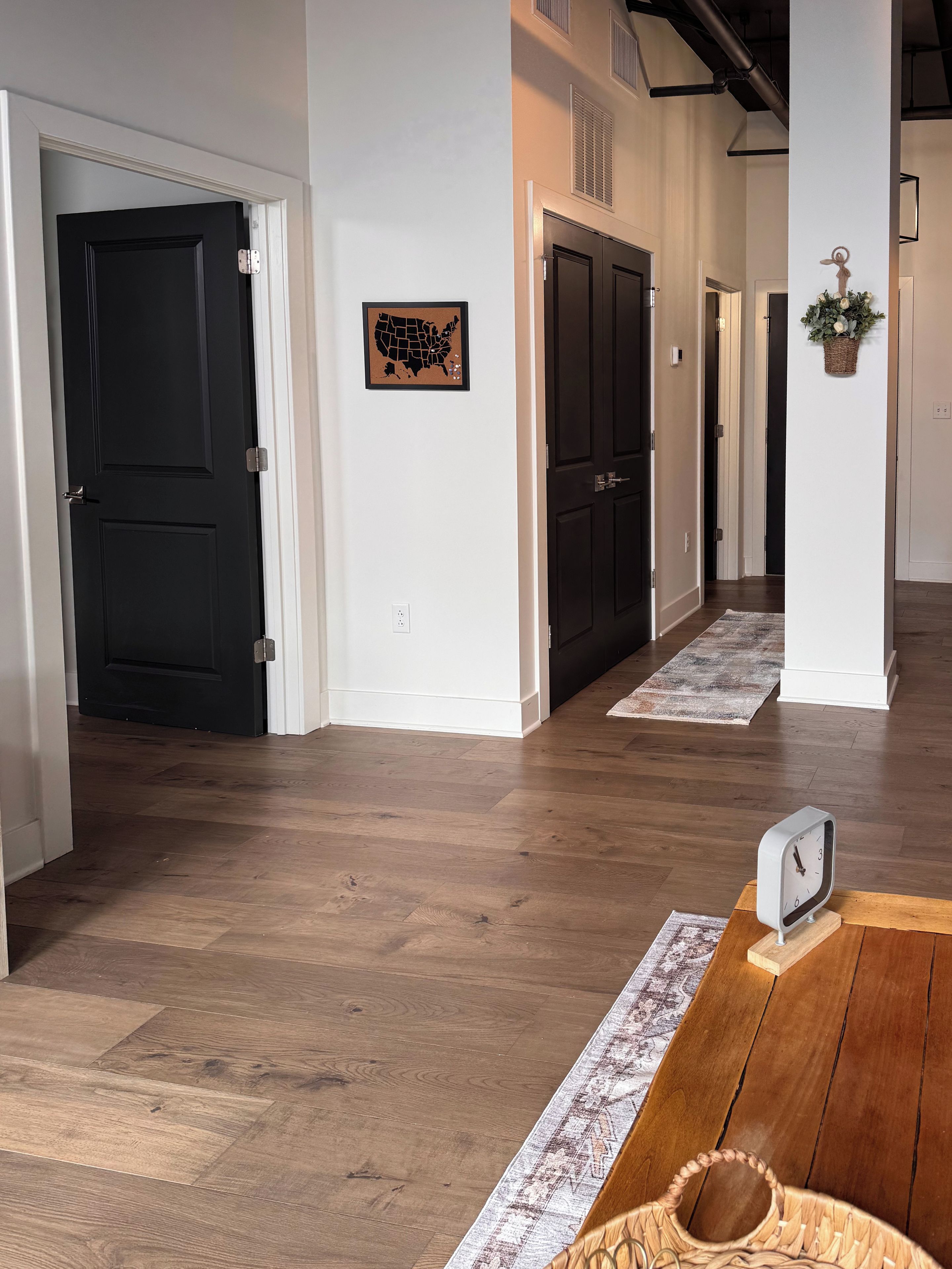 A hallway with wooden flooring, black doors, a wall-mounted map, and a clock.