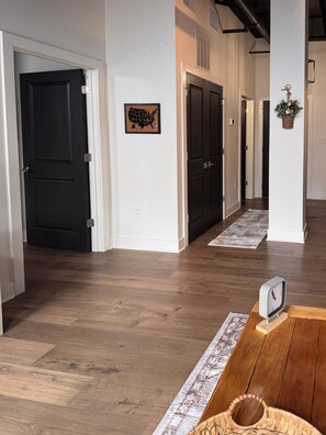 Un corridoio con pavimento in legno, porte nere, una mappa appesa al muro e una sveglia.