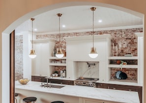 Une cuisine dotée d’un plan de travail en marbre, d’un mur en briques et de luminaires suspendus.