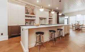 A modern kitchen with a large island, bar stools, and pendant lighting.