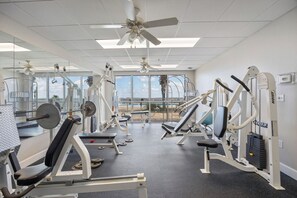 A gym with ceiling fans, exercise equipment, and large windows with a view. - BYO Boat! 2BR Waterfront Condo (Pensacola)