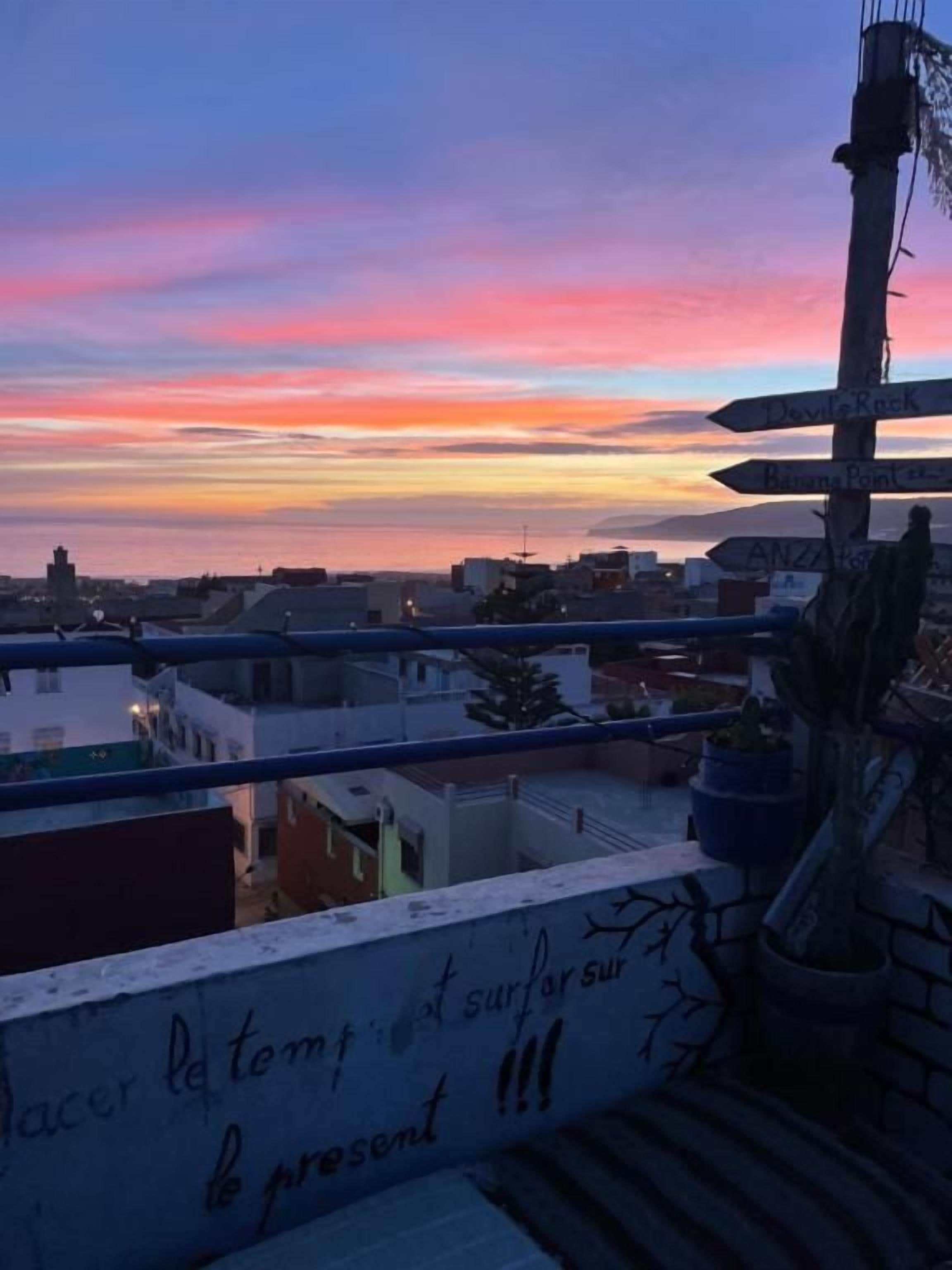 A balcony with a view of a sunset over a cityscape, a directional sign, and some graffiti.