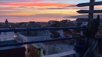 Un balcón con vista a un atardecer sobre el paisaje urbano, una señal de indicaciones y algunos grafitis.